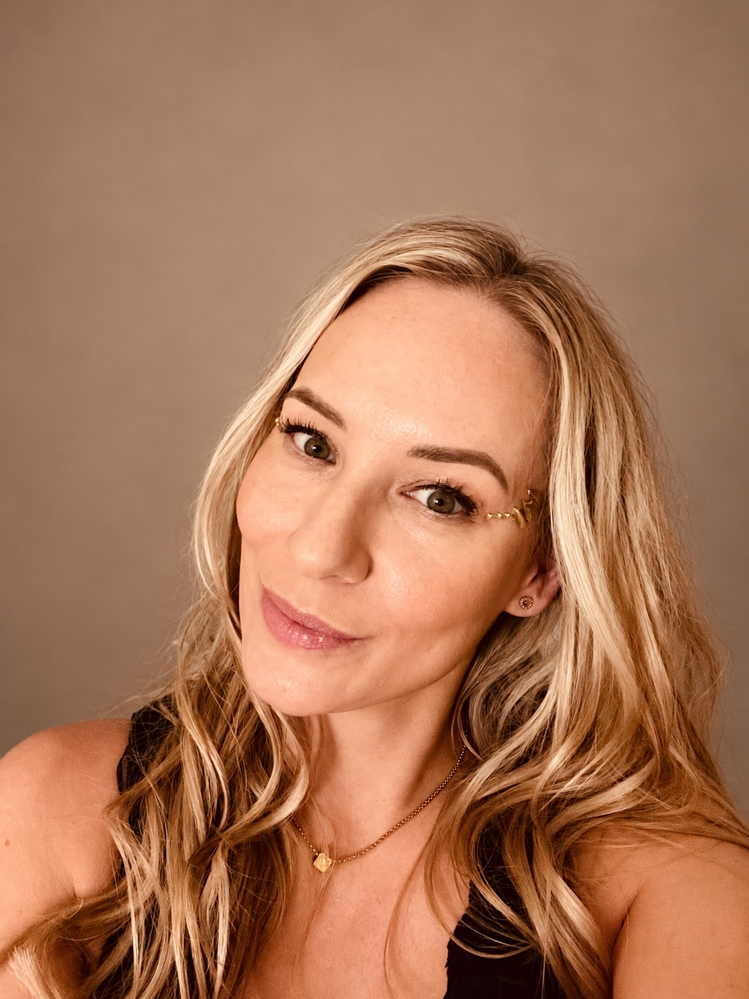 Sandra with loose blonde waves, a black top and small gold details beside her eyes