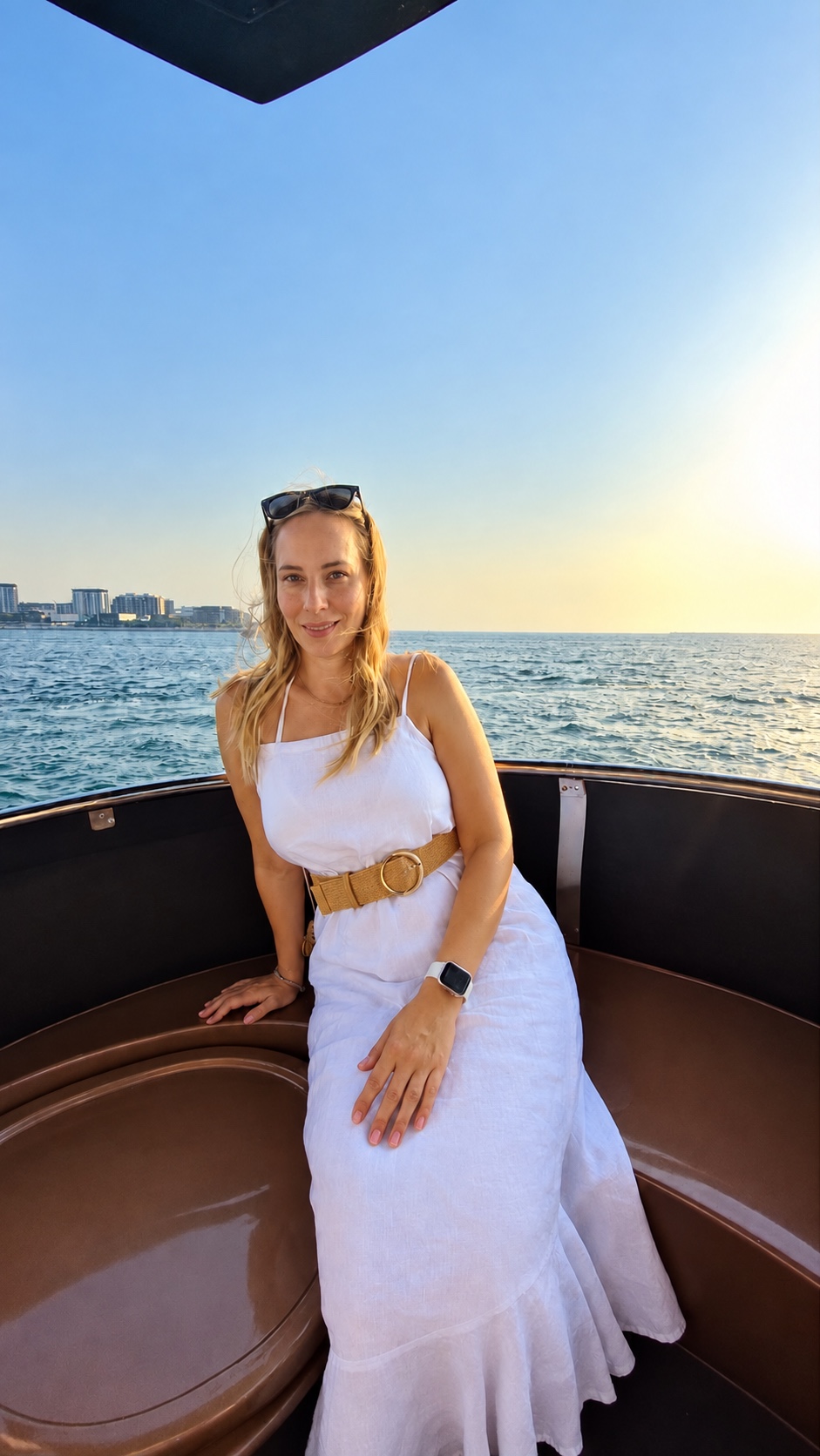 Sandra seated on a boat in a white dress, with the sea behind her