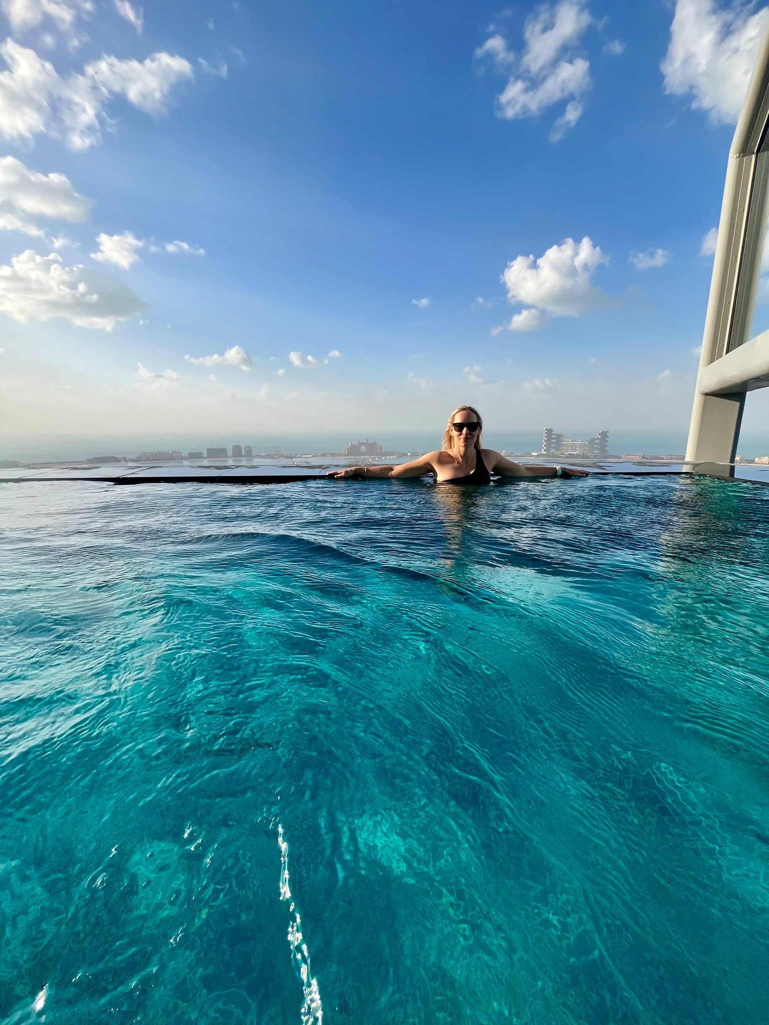 Sandra in an infinity pool beneath a wide blue sky, with the coast in the distance